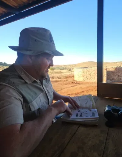 Photo of a man sitting on a patio, reading a book.